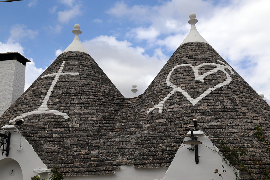 Alberobello.
Certains trulli ont le toit dÃ©corÃ© de motifs aux origines mystÃ©rieuses : roues solaires, lunes, candÃ©labres, cÅ“ur dans un triangle... Mais la signification de ces symboles semble avoir Ã©tÃ© oubliÃ©e au cours des siÃ¨cles.